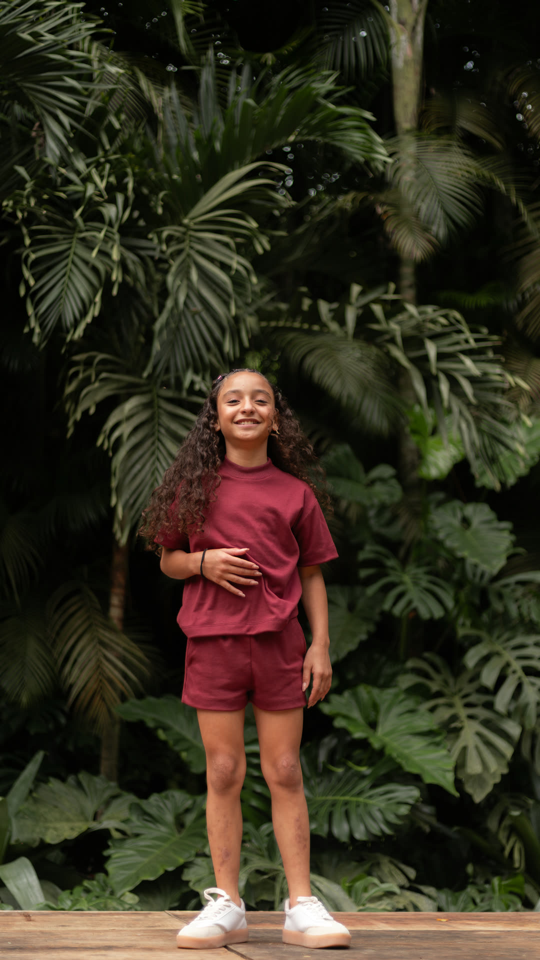 Menina sorrindo no jardim com o conjunto Banim Bordô